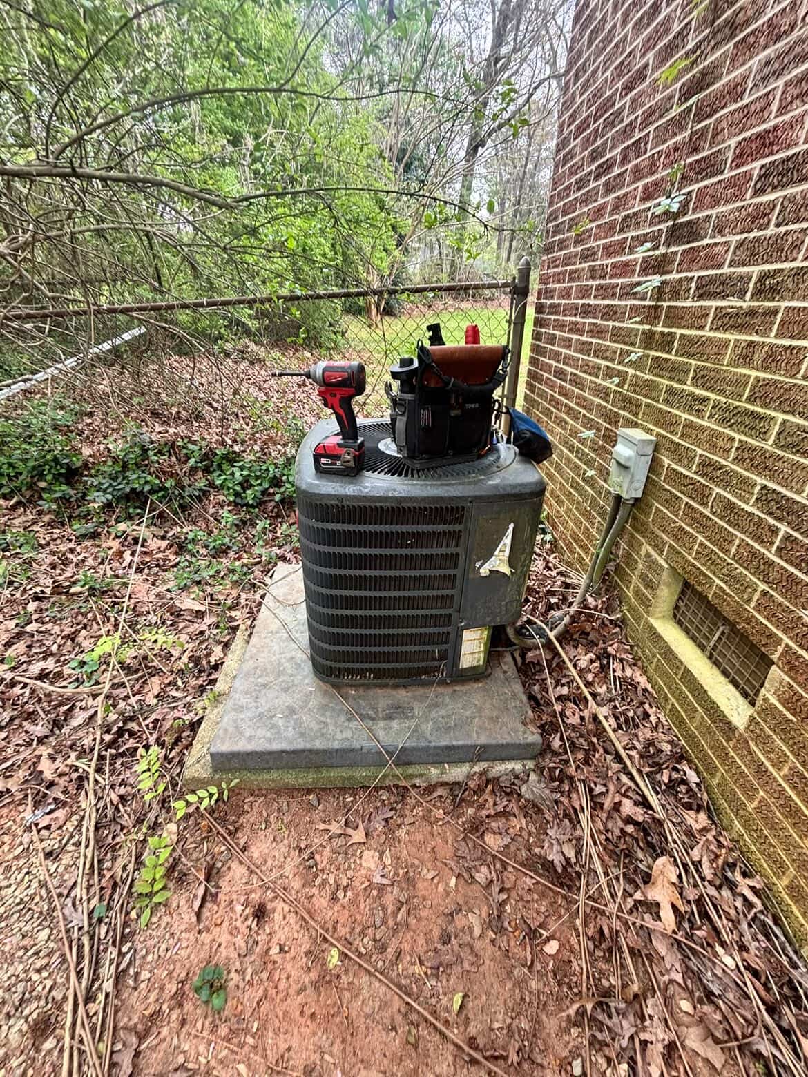 HyperTemp HVAC servicing an outdoor AC condenser beside a brick home